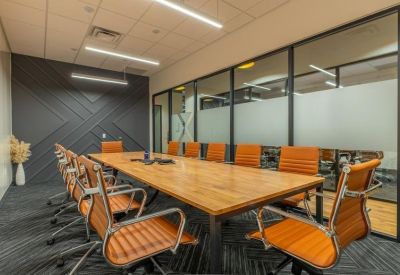 Spacious boardroom with a long wooden table, orange chairs, and natural light from glass walls.