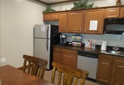 Office kitchen area with wooden cabinets, stainless steel refrigerator, microwave, and a dining table.