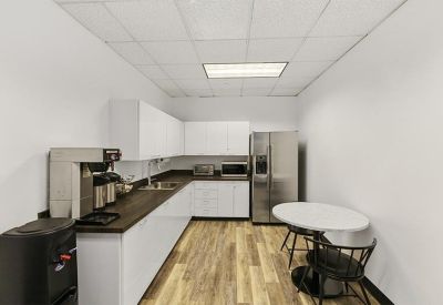Bright communal kitchen with white cabinetry, a wood-style floor, and a small dining table.