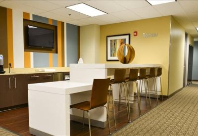 Modern breakroom with a high-top white table, breakfast bar, and wall-mounted television.