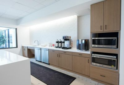 Modern office breakroom featuring wood cabinetry, microwaves, and coffee station.