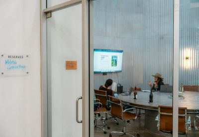 Glass-walled conference room with a large round table and wall-mounted display screen.