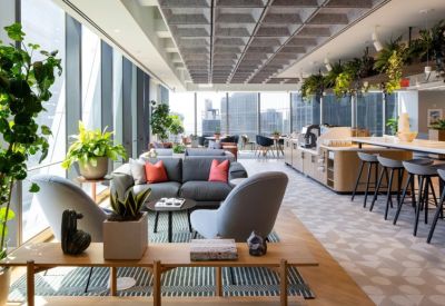 Lounge area with plush grey seating, colorful pillows, and large windows overlooking the city.