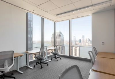 Bright corner office space with light wood desks and ergonomic chairs facing floor-to-ceiling windows.