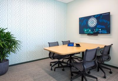 Small meeting room featuring a light wood table, mesh chairs, and a screen against patterned wallpaper.