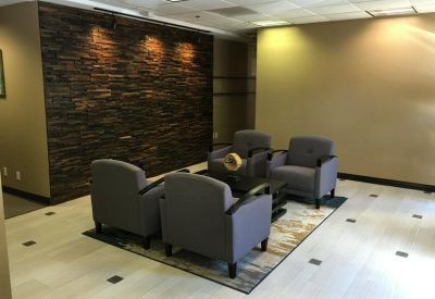 Modern lobby area with grey armchairs, a rug, and a dark stone-textured feature wall.