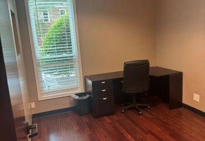 Private office with wood-look flooring, a large window, and an L-shaped desk.