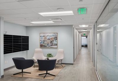 Lounge area with blue and white chairs, a black coffee table, and a hallway lined with offices.
