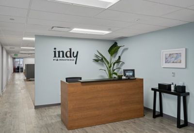 Bright reception area with a wood-paneled desk, branded wall signage, and a potted plant.