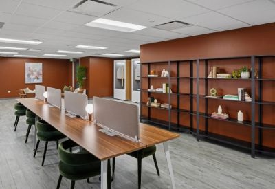 Coworking space featuring long wooden desks, green velvet chairs, and a rust-colored feature wall.