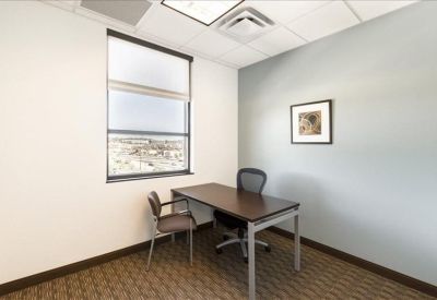 Private corner office with a dark wood desk and city view from a large window.