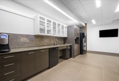 Modern office kitchen with wood-look flooring, dark cabinetry, and white glass-front cupboards.