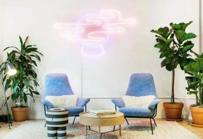 Breakout lounge featuring blue armchairs, a pink neon cloud sign, and potted plants.
