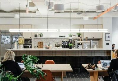 Bright office kitchen and dining area with long tables and modern industrial lighting.