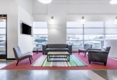 Bright communal lounge area with gray armchairs and a colorful striped rug.