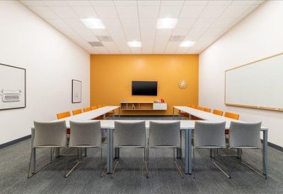 Coworking space with multiple wooden dining-style tables and grey chairs under a warm wood ceiling.