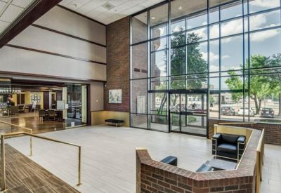 Spacious sun-lit lobby with high glass walls and a modern brick seating area.