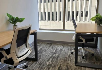 Private office space with a large window and wooden desks featuring potted green plants.