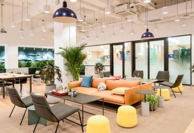 Spacious modern lounge with an orange sofa, yellow ottomans, and indoor plants.