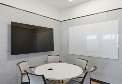 Small four-person meeting room with a wall-mounted screen and dry-erase board.