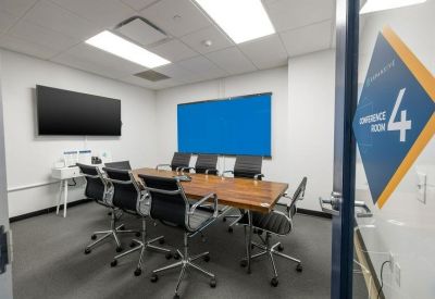 Boardroom with a wooden table, black leather chairs, and a large wall-mounted screen.