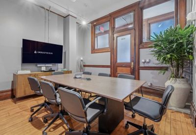 Modern conference room with a wooden table, wall-mounted screen, and large potted plant.