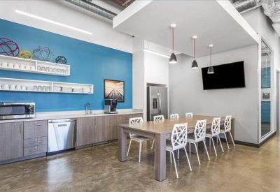 Bright breakroom featuring a blue tiled backsplash, wooden cabinets, and a large dining table.