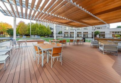 Spacious outdoor wooden deck with patio dining sets under a slatted pergola.