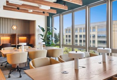 Bright coworking space with warm wood ceiling beams, yellow armchairs, and large windows.