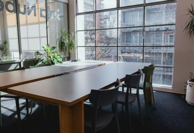 Private meeting area with a long wooden table, green chairs, and large industrial-style windows.