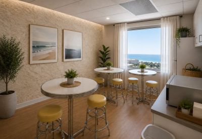 Breakroom with round cafe tables, yellow stools, and an ocean-view window.