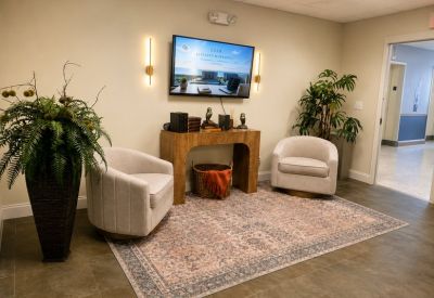 Lounge area with two cream armchairs, a patterned rug, and wall-mounted TV.