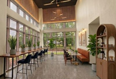 Bright coworking area with high ceilings, large windows, a long bar counter, and orange booth seating.