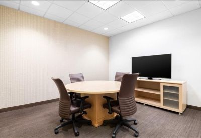 Small meeting room with a round wooden table, four chairs, and a wall-mounted TV.