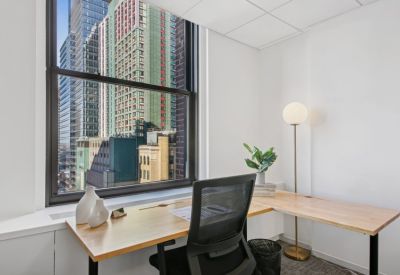 Sunlit private corner office with a wooden desk and views of skyscrapers.