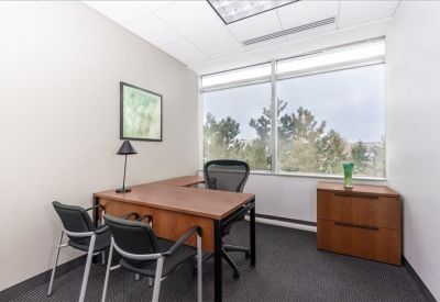 Private office featuring an L-shaped wooden desk and a window overlooking greenery.