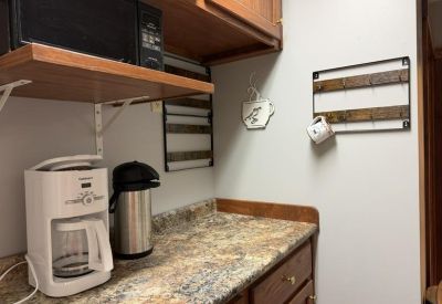 Office kitchen area with a coffee maker, microwave, and wooden cabinetry.