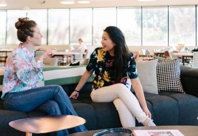 Two women conversing on a modern dark blue sectional sofa in a bright breakout area.