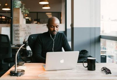 Professional at a laptop in a modern office setting with warm overhead lighting and a black mug.