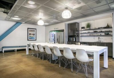 Bright communal kitchen and dining area with a long white table and designer Eames-style chairs.