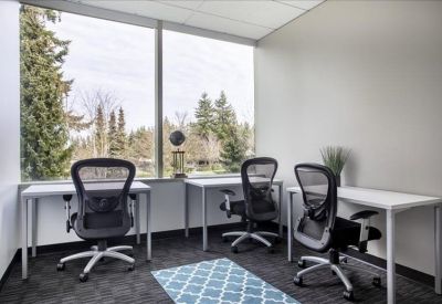 Bright office with three black ergonomic chairs and large windows overlooking trees.