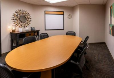 Small conference room featuring an oval wood table, black chairs, and a decorative sunburst mirror.