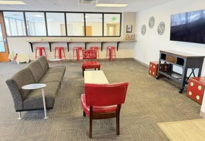 Modern lounge area with a grey sofa, red chairs, and a breakfast bar with red stools.