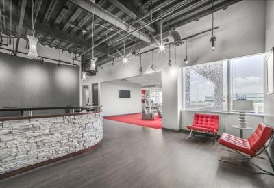 Lounge area with red designer chairs and an industrial-style ceiling near a stone-faced desk.