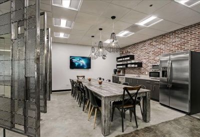 Communal breakroom with a large rustic table, brick accent wall, and stainless steel fridge.
