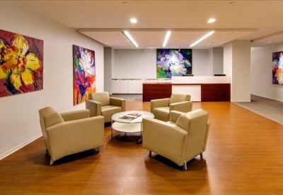 Bright reception area with wood floors, tan armchairs, and colorful floral artwork.