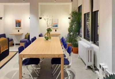 A long wooden communal table with blue chairs in a bright meeting area.