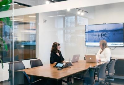 Modern meeting room with two people at a wooden table using laptops in front of a large screen.
