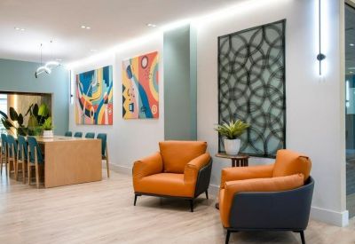 Reception area with orange chairs, colorful art, and a geometric feature wall.