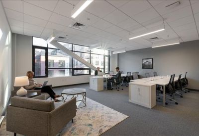 Spacious open-plan coworking area with lounge seating and workstations near large windows.